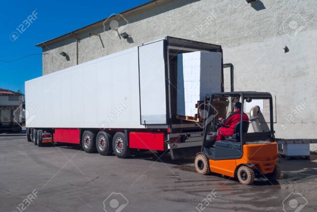 Worker on the loader unload white semi-trailer
